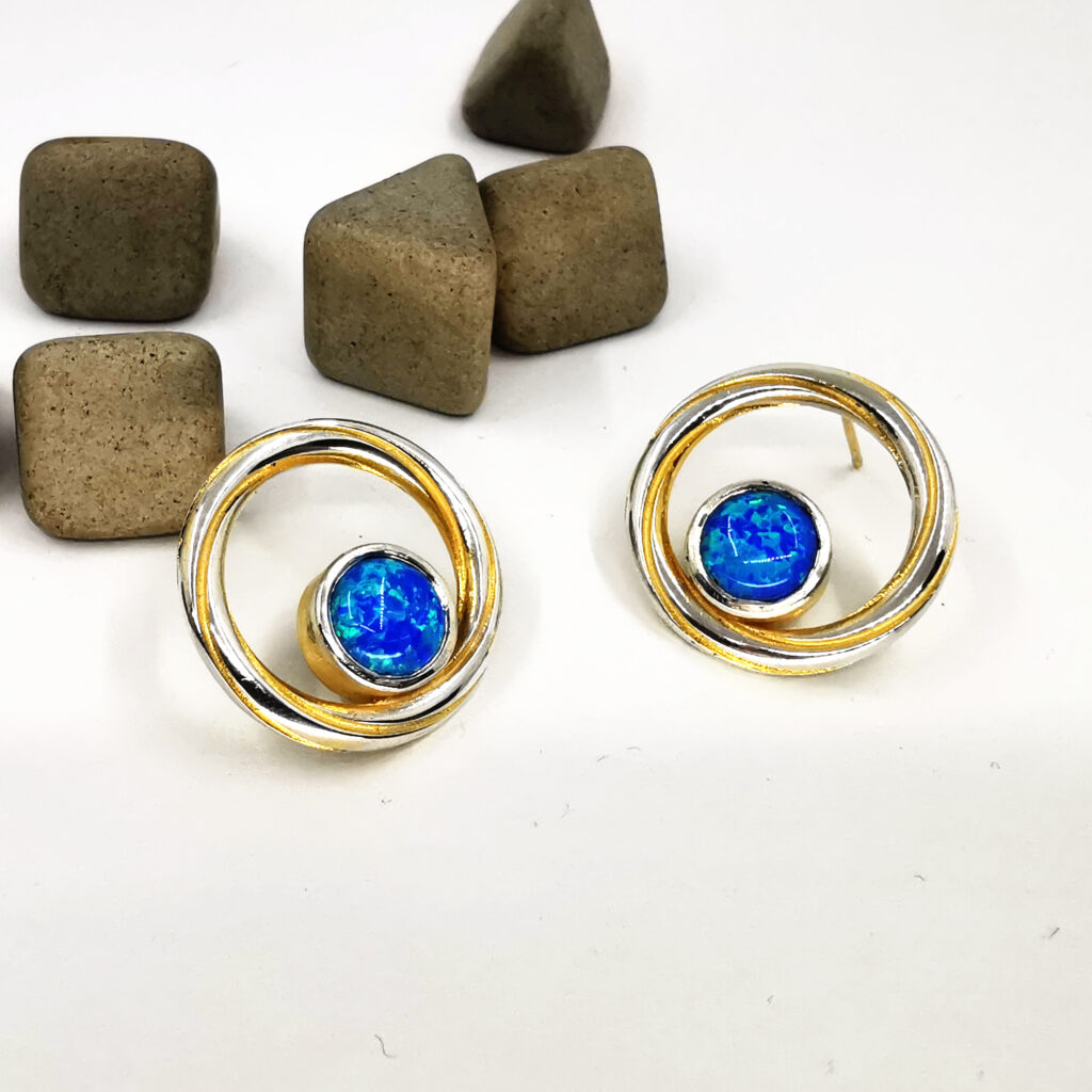 Handmade Twist Continuum earrings in sterling silver with gold plated detailing and vivid blue green lab grown opal cabochon stones set within a circular design