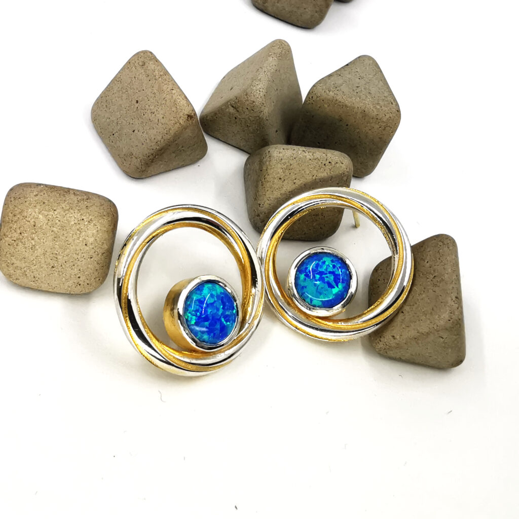 Handmade Twist Continuum earrings in sterling silver with gold plated detailing and vivid blue green lab grown opal cabochon stones set within a circular design
